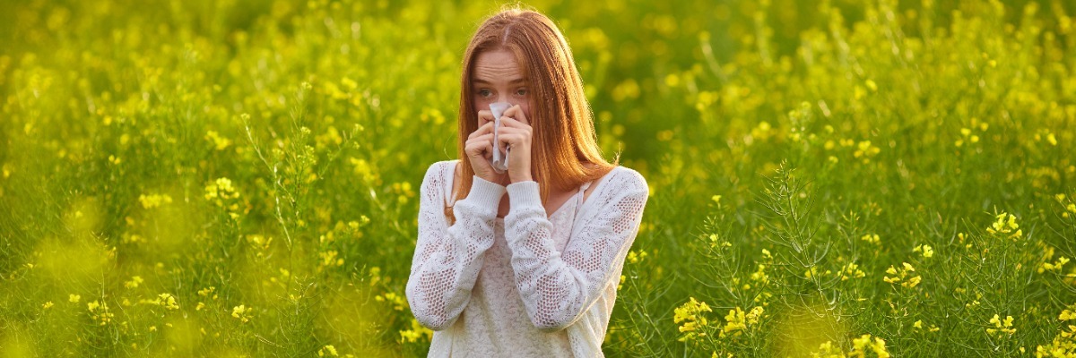 Woman blowing her nose in a field with yellow flowers