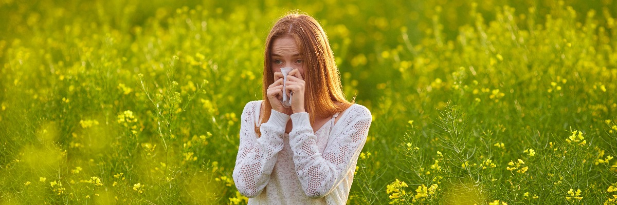 Woman with dry eye or hayfever blows her nose in a field 