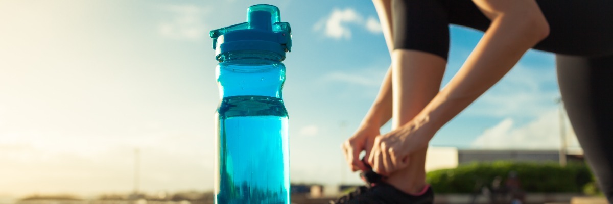 Water Bottle sits in the foreground as a woman ties her trainers in the background 